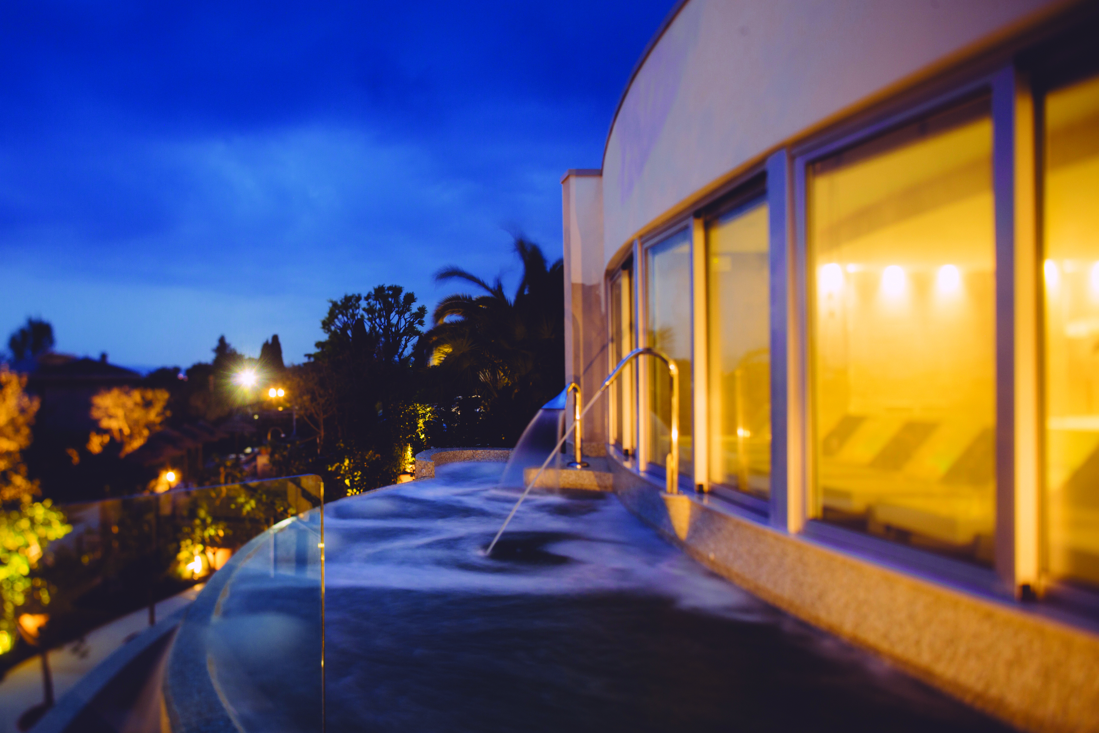 View of the thermal pool at dusk with lights lit up and water being sprayed into the pool