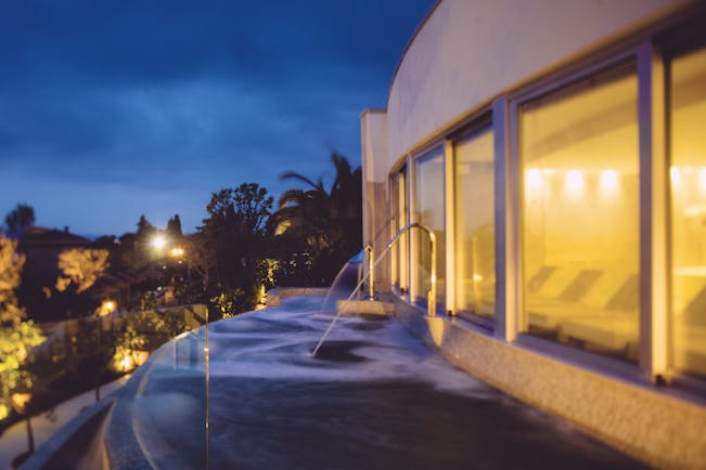 View of the thermal pool at dusk with lights lit up and water being sprayed into the pool