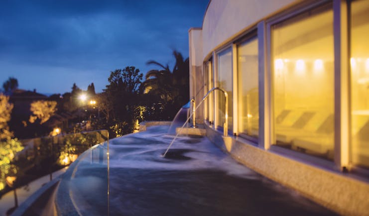 View of the thermal pool at dusk with lights lit up and water being sprayed into the pool