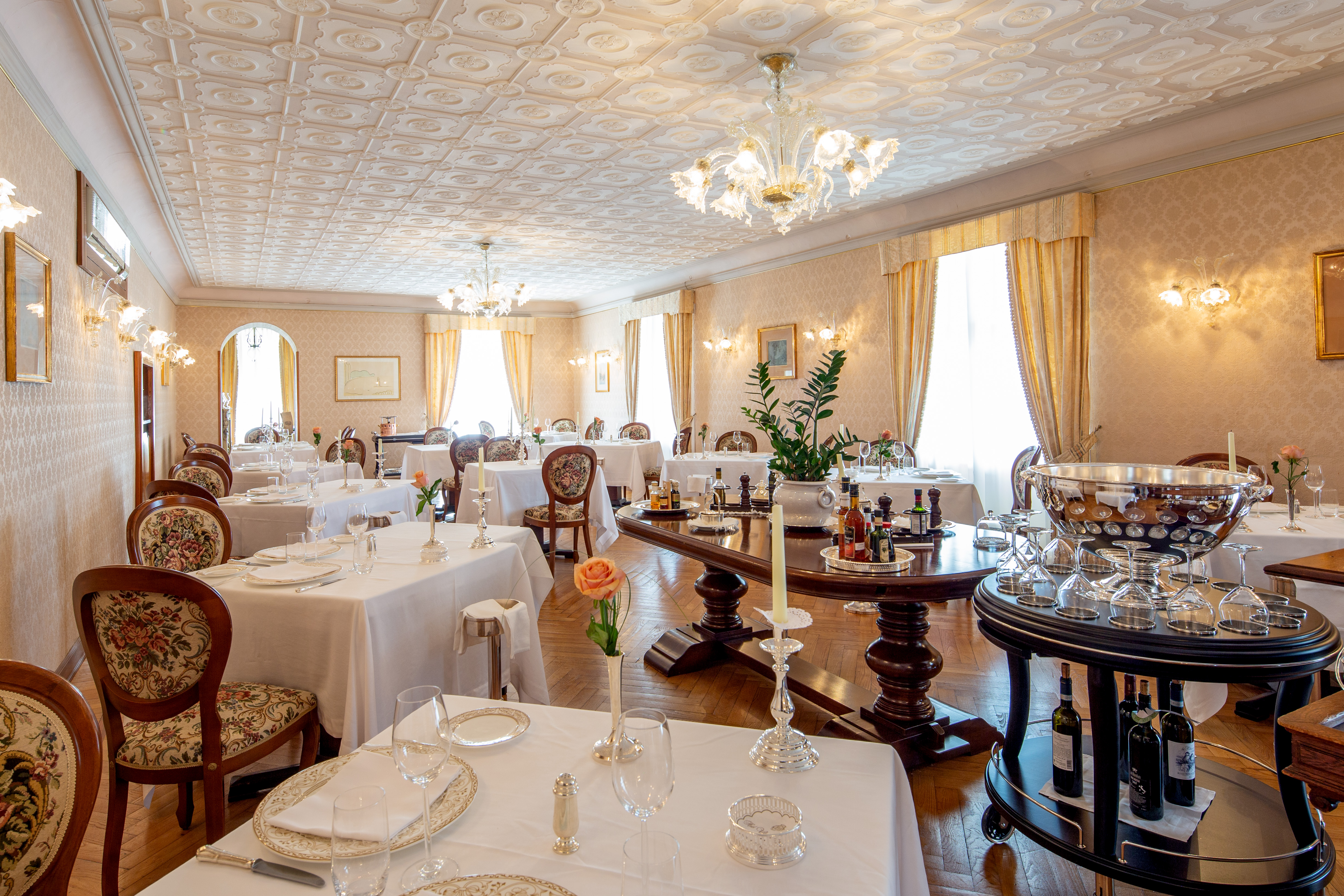 Restaurant with tables and chairs set up for dining in large white room with chandeliers