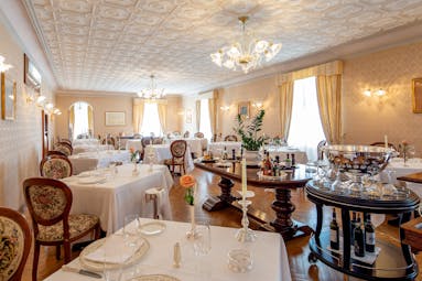 Restaurant with tables and chairs set up for dining in large white room with chandeliers