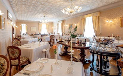 Restaurant with tables and chairs set up for dining in large white room with chandeliers