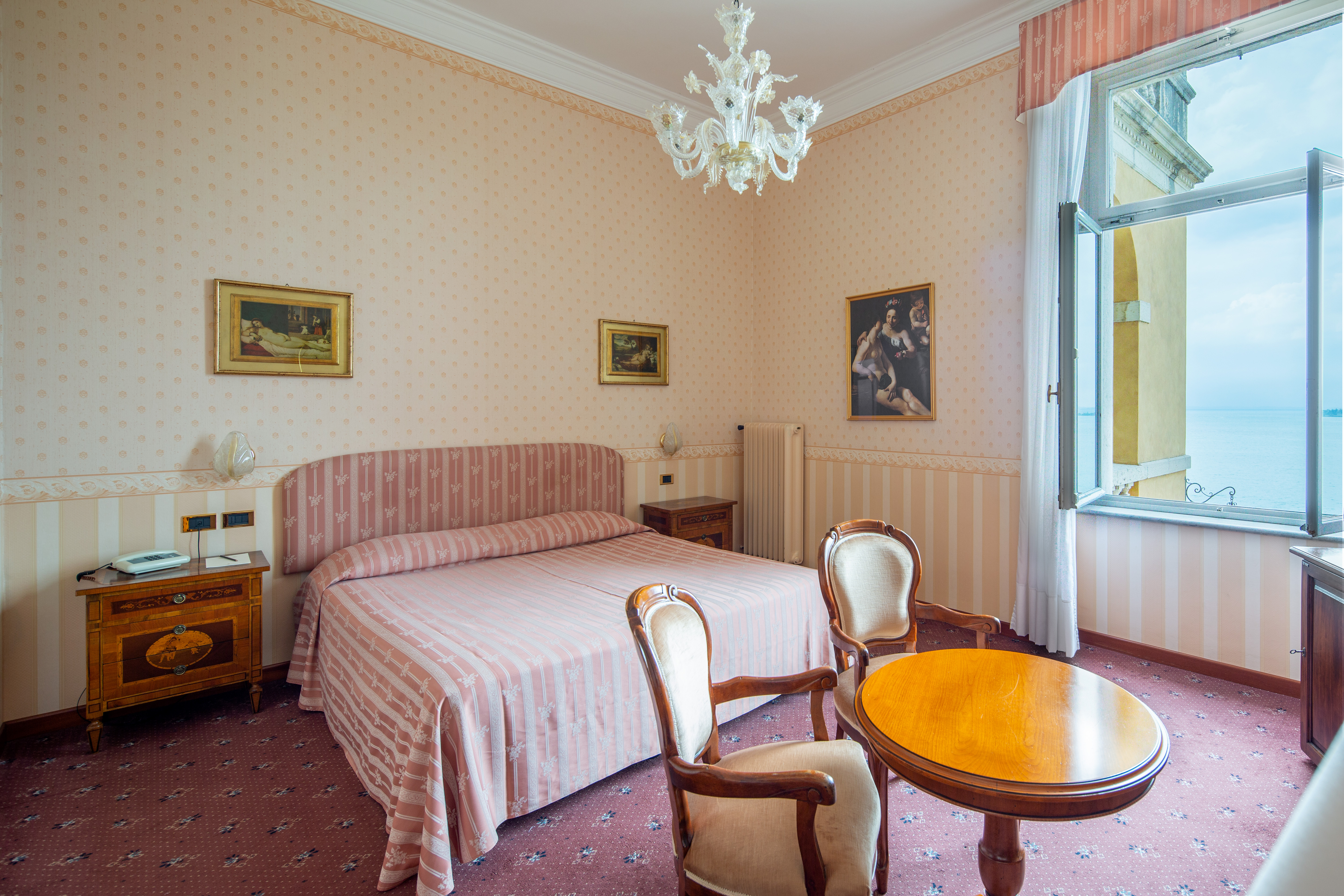 Standard room with chandelier, double bed, windows and artwork on the walls