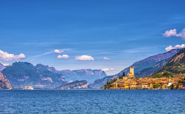 Orange coloured town of Malcesine perched on shore of blue waters of Lake garda with mountains