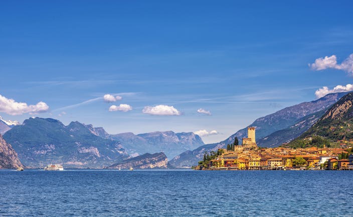 Orange coloured town of Malcesine perched on shore of blue waters of Lake garda with mountains