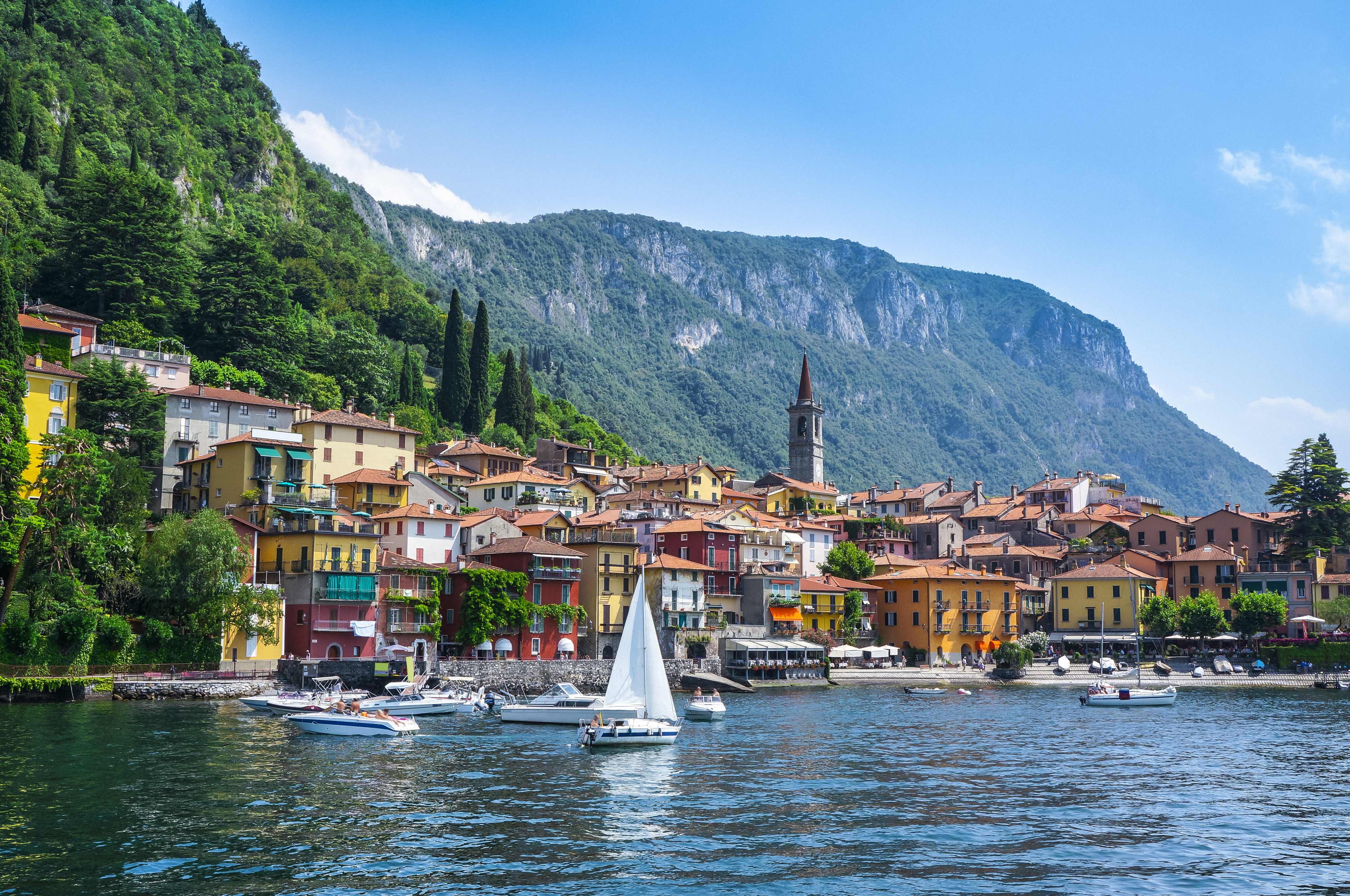 Sailing boat on deep blue water of lake como with town of Varenna on the shore
