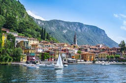 Sailing boat on deep blue water of lake como with town of Varenna on the shore