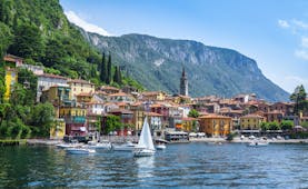 Sailing boat on deep blue water of lake como with town of Varenna on the shore