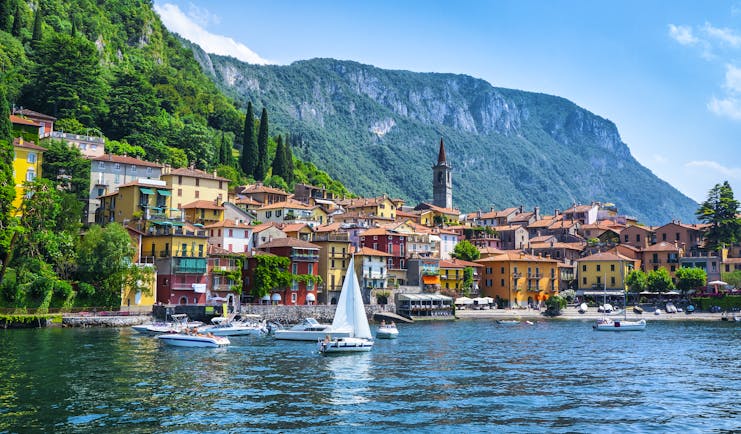 Sailing boat on deep blue water of lake como with town of Varenna on the shore