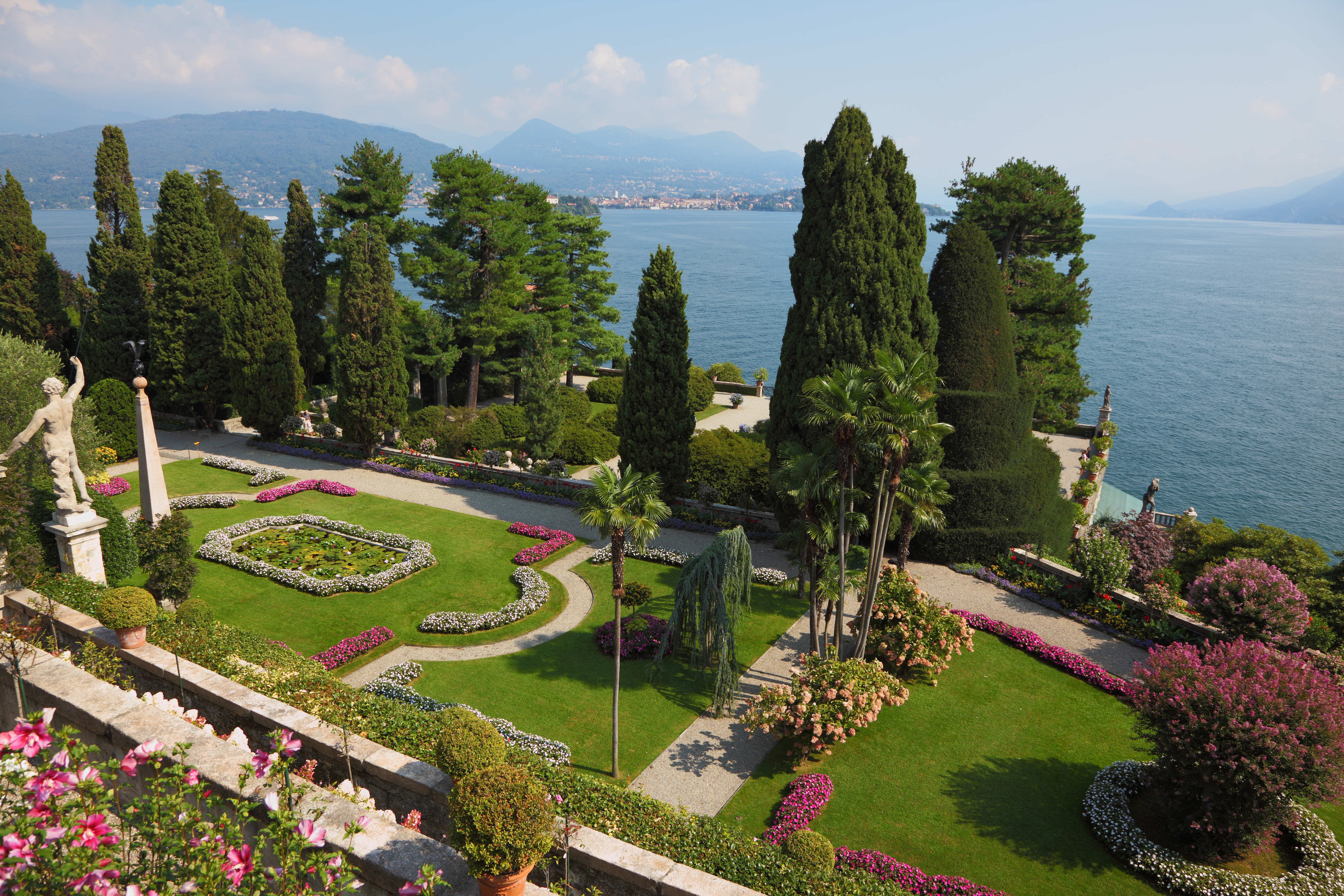 Terraced grassy gardens and stone walls with red flowers overlooking lake como