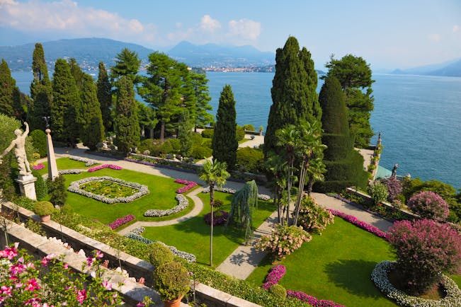 Terraced grassy gardens and stone walls with red flowers overlooking lake como