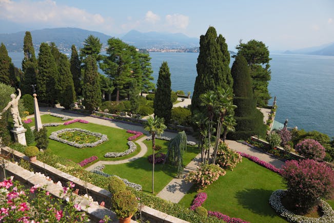 Terraced grassy gardens and stone walls with red flowers overlooking lake como