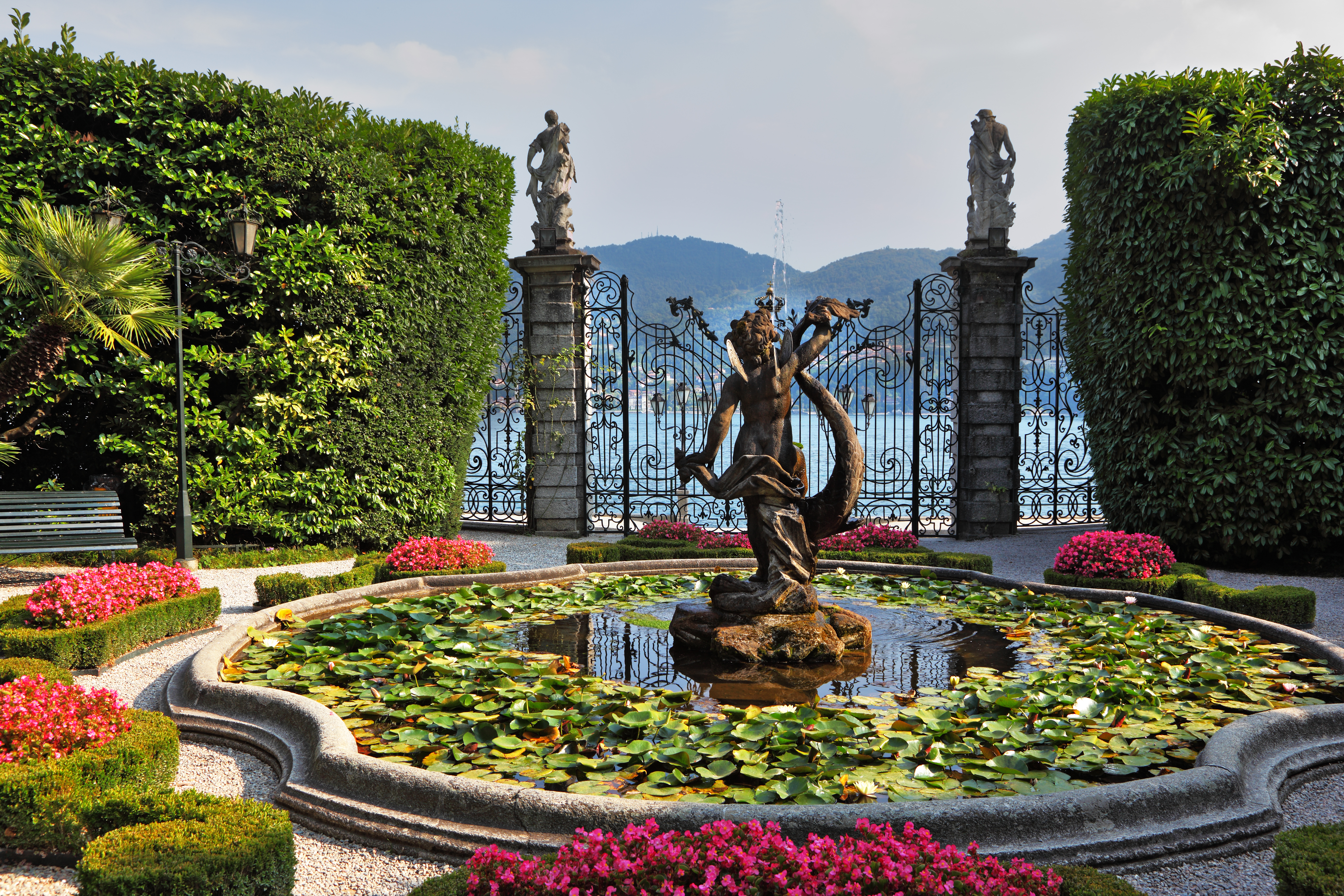 Fountain and pond with water lilies and pots of red flowers by gate at Villa Carlott on Lake Como