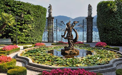 Fountain and pond with water lilies and pots of red flowers by gate at Villa Carlott on Lake Como