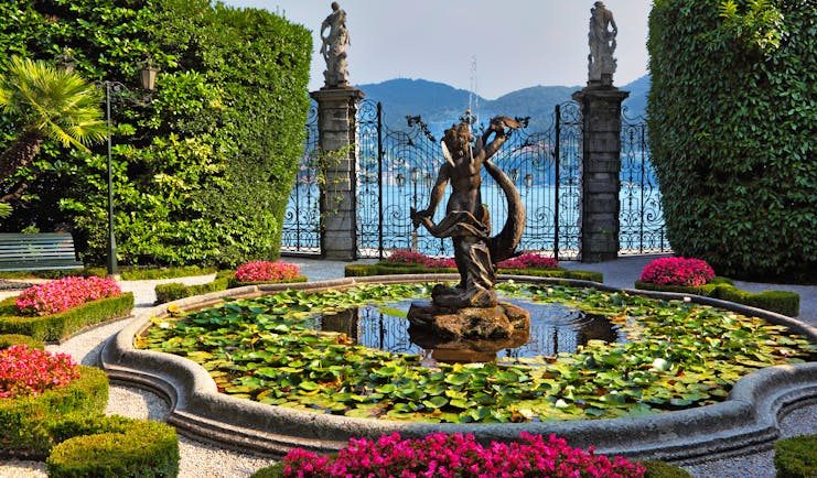 Fountain and pond with water lilies and pots of red flowers by gate at Villa Carlott on Lake Como