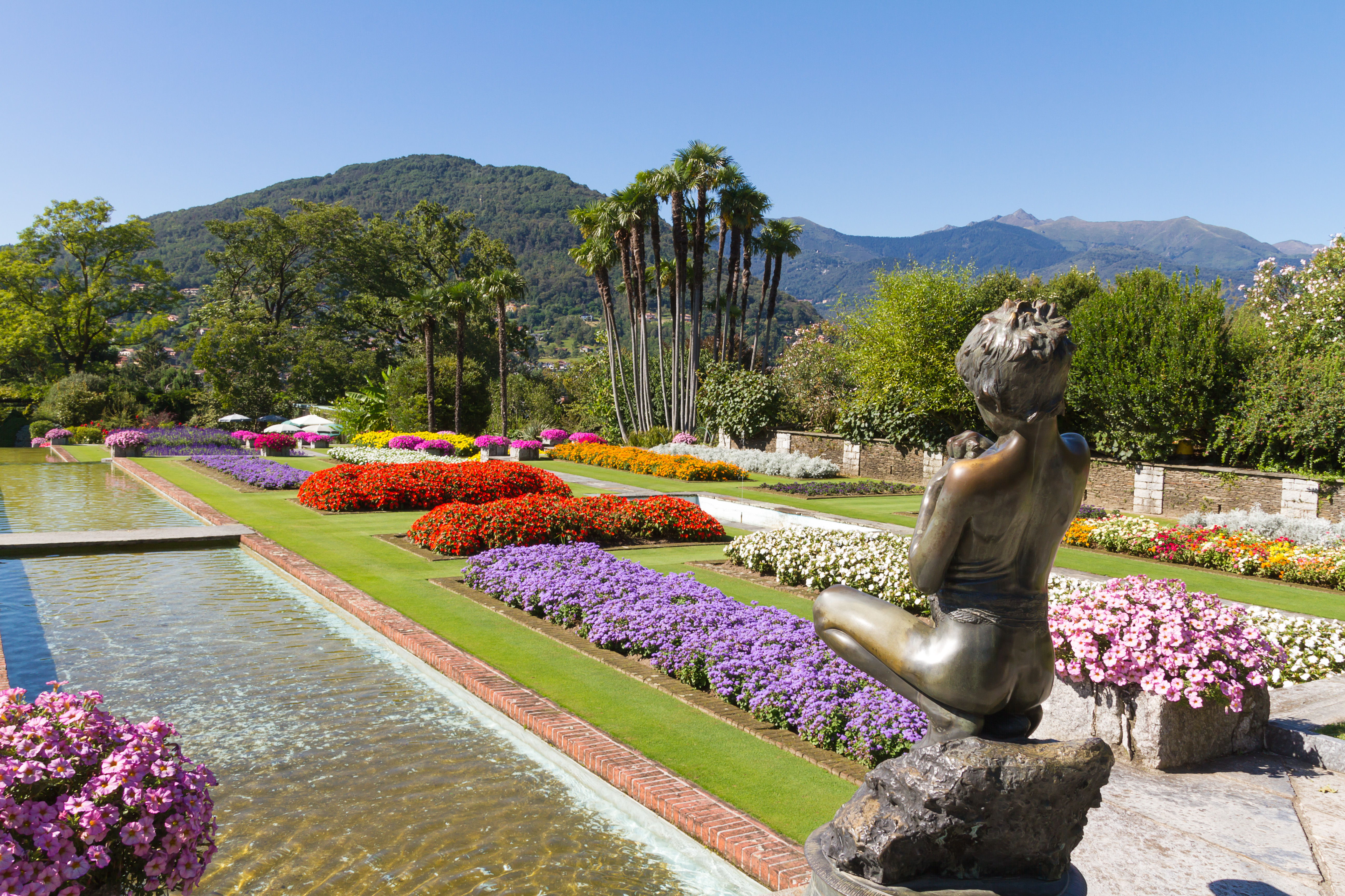 Statue of girl overlooking water feature with colourful summer flowers in borders at Villa Taranto on Lake Maggiore
