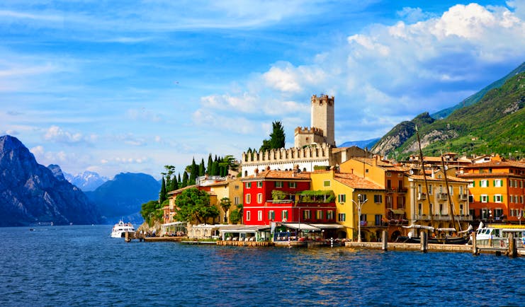 Sunlight village with castle tower on edge of deep blue Lake Garda