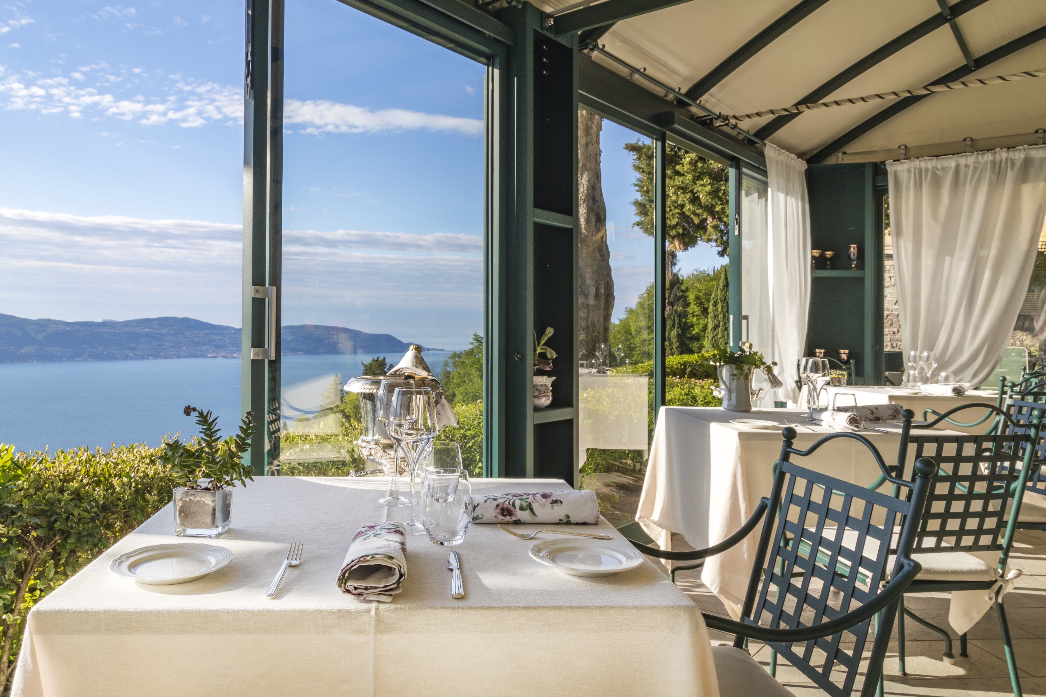 Villa Sostaga breakfast dining with wrought iron chairs and white-clothed tables overlooking lake views