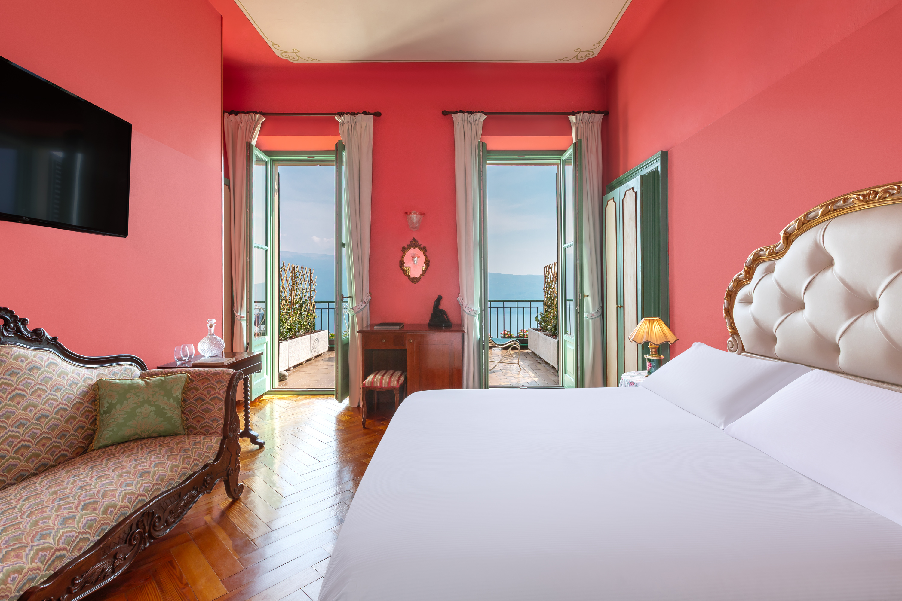 Villa Sostaga Signature Room with cheerful pink decor, antique furnishings, and doors leading out onto a lake view terrace