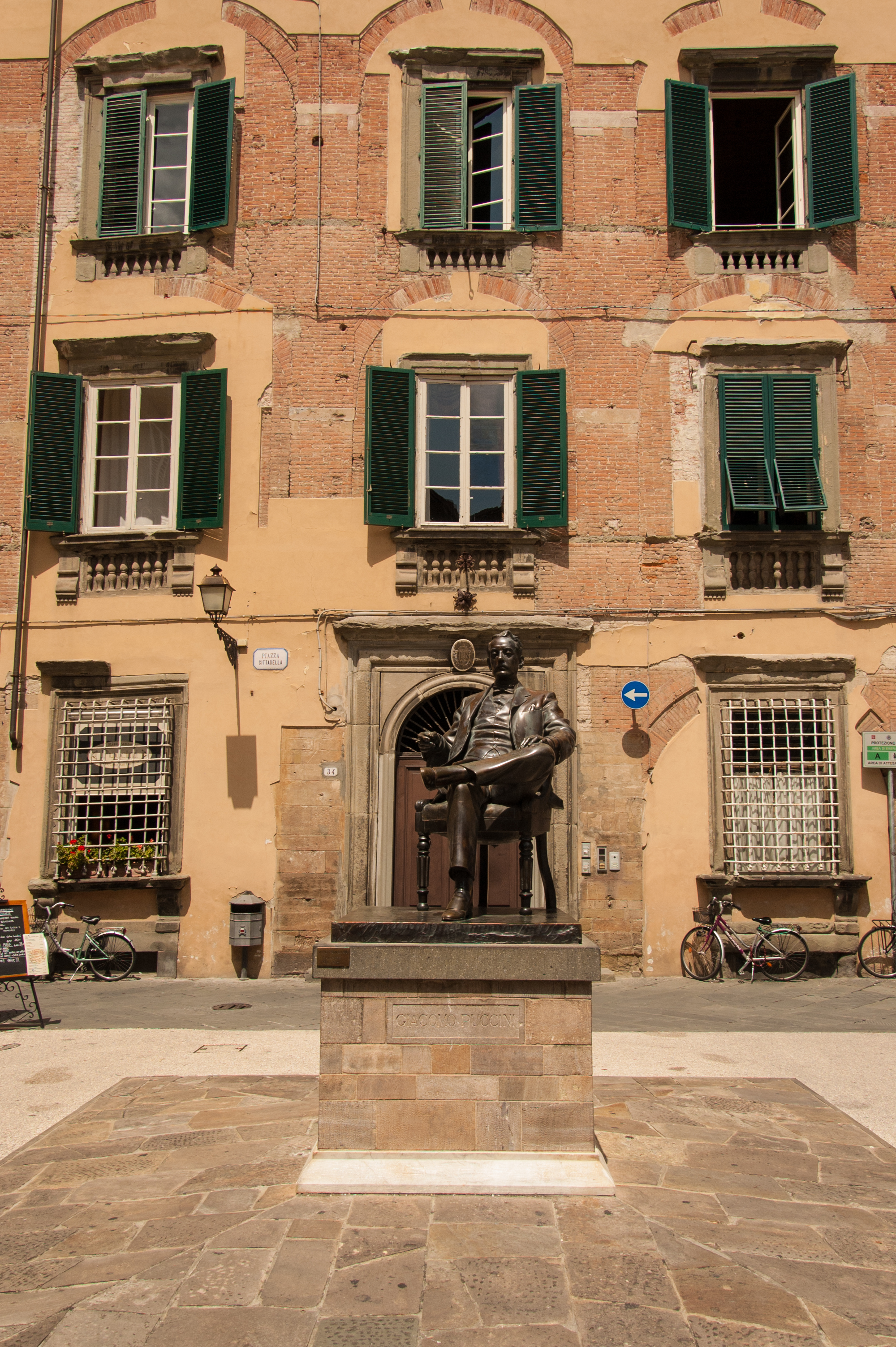 Statue of composer Puccini in front of punk and green building in Lucca