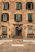 Statue of composer Puccini in front of punk and green building in Lucca