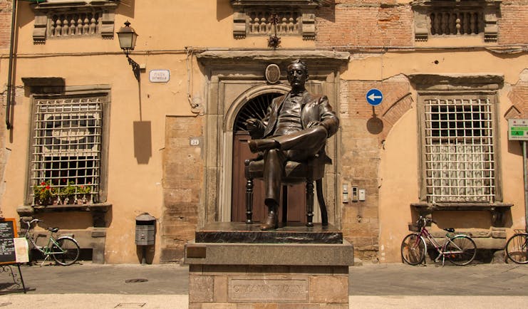 Statue of composer Puccini in front of punk and green building in Lucca