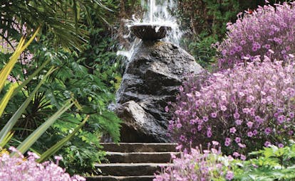 Fountain with statue high up on a stone staircase bordered by pink flowers