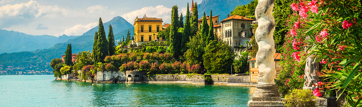 Ochre villa on side of lake with terraced gardens of red flowers