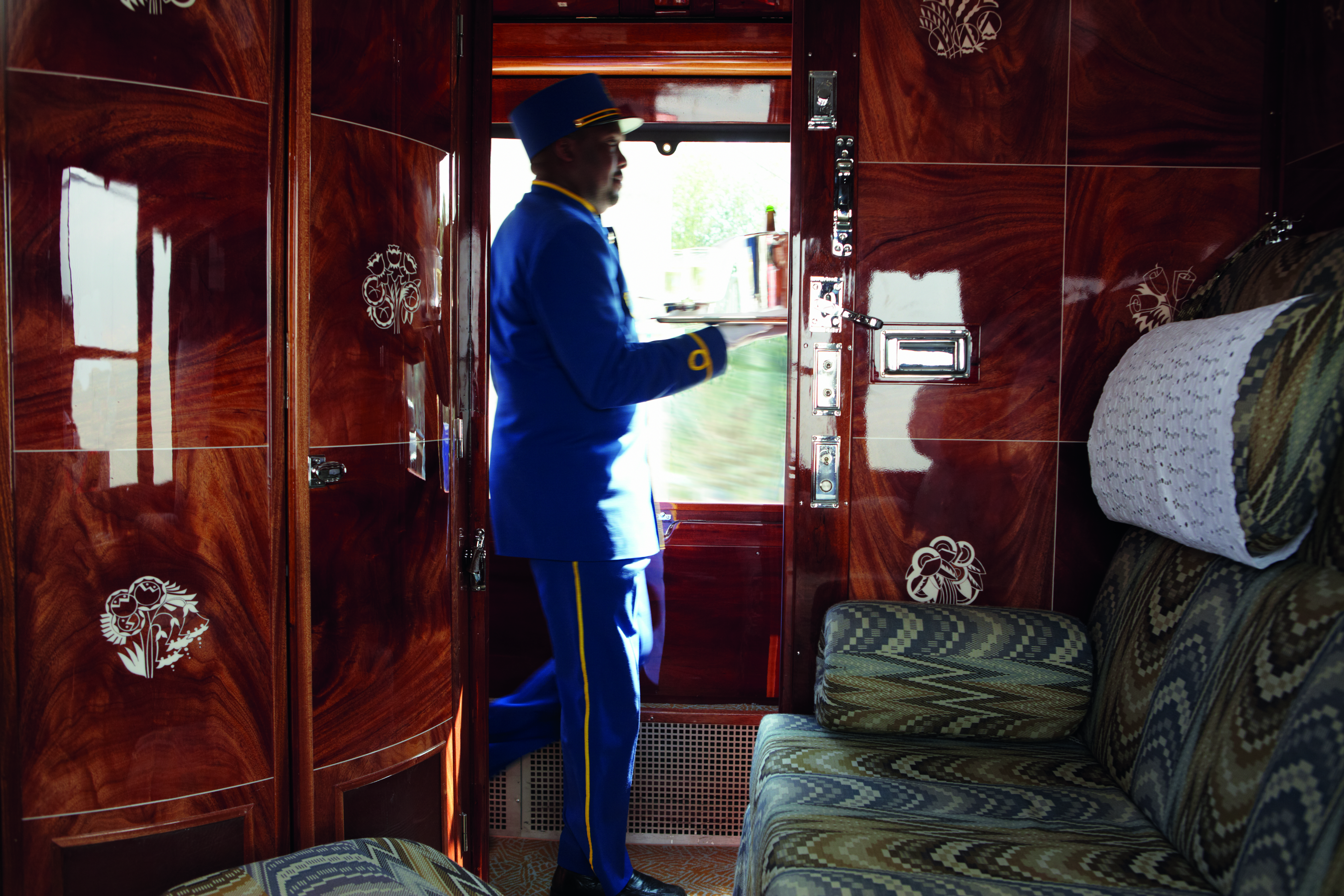 Shiny wooden train cabin with large seat and waiter with drinks on the Orient Express
