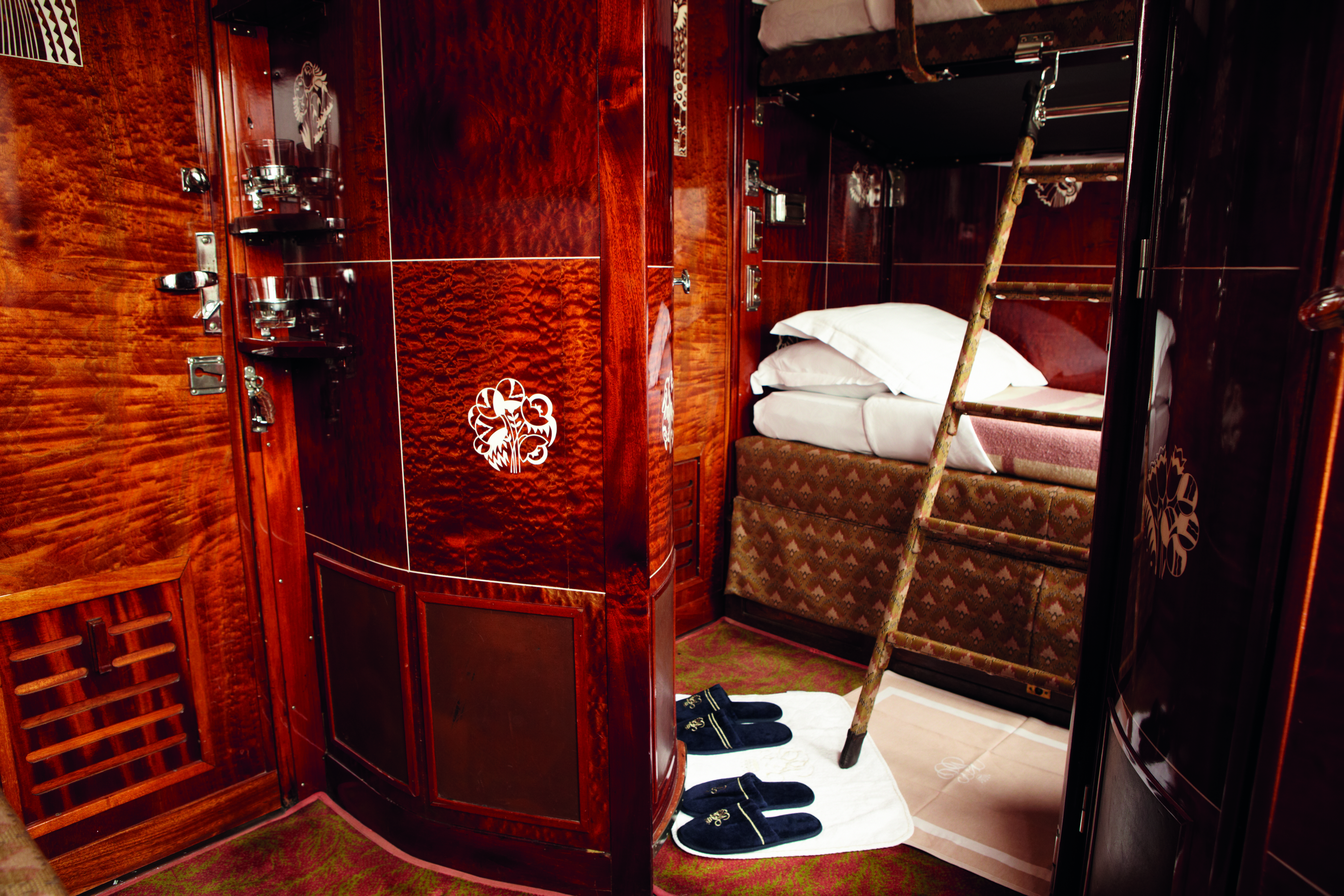 Dark shiny wooden railway cabin with bed and ladder on Orient Express
