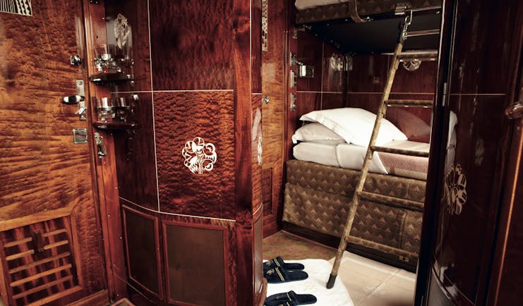 Dark shiny wooden railway cabin with bed and ladder on Orient Express