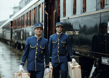 Two porters in blue uniform carrying suitcases on the Orirent Express