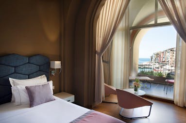 Junior suite with double bed, arm chairs and doors opening onto a terrace areas with views over city and ocean 