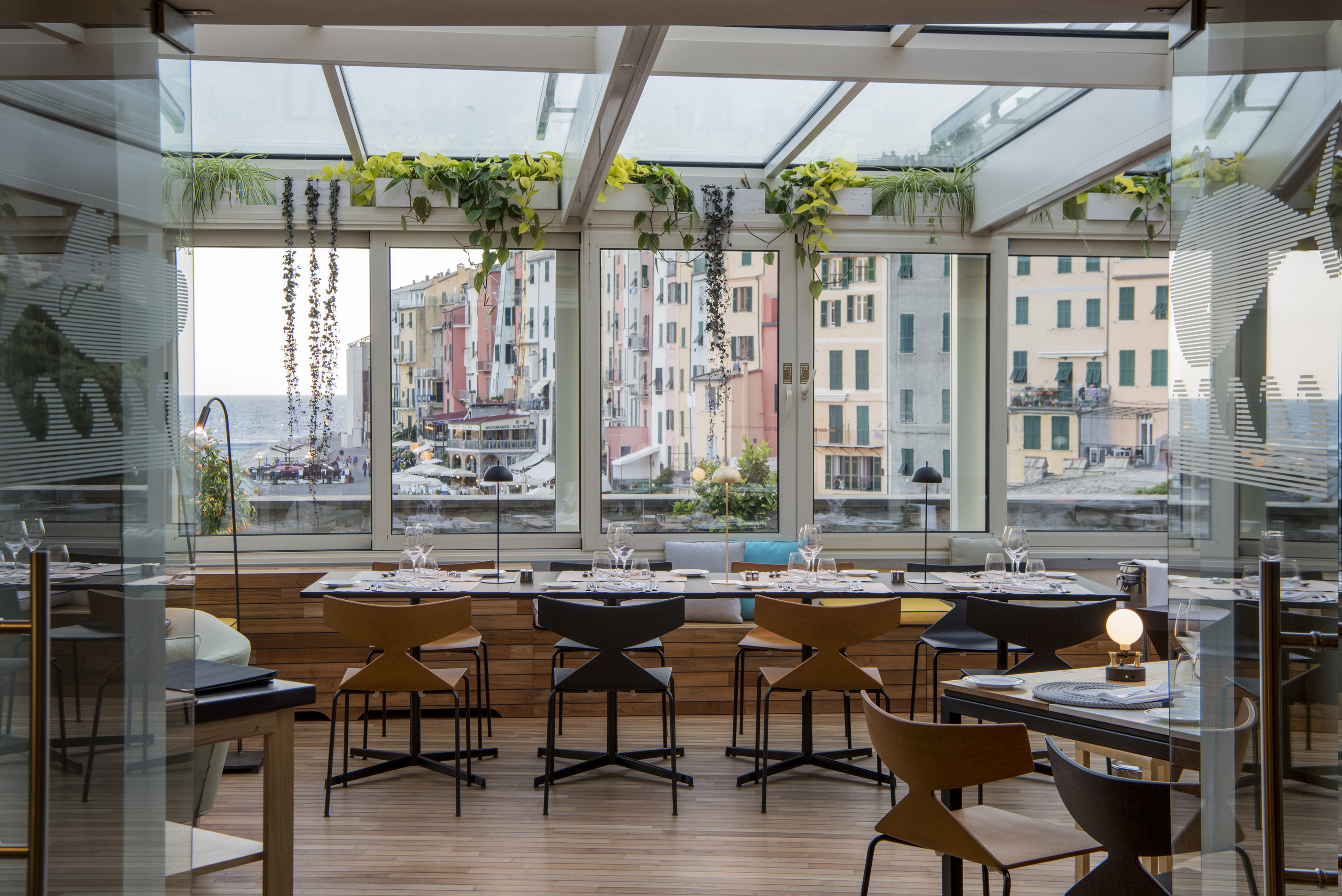Restaurant with glass windows and walls looking over the port, and tables and chairs set up for dining inside
