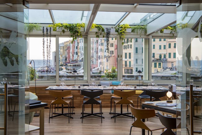 Restaurant with glass windows and walls looking over the port, and tables and chairs set up for dining inside