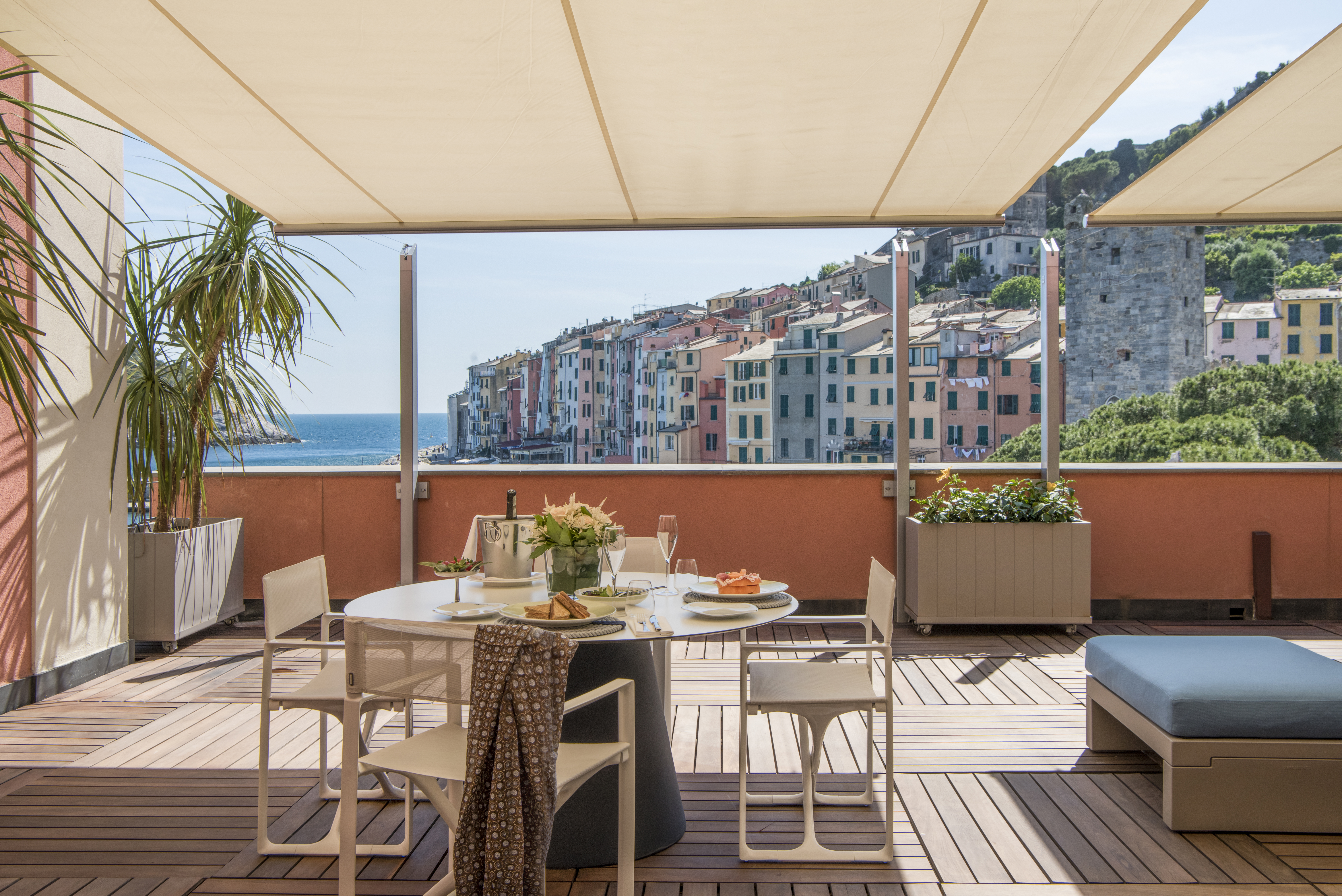 Terrace outdoor covered dining area with tables and chairs set out on wooden decking with views over ocean and colourful  buildings 