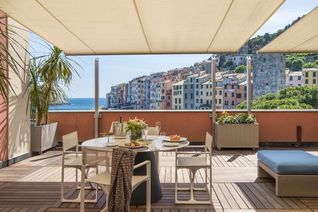 Terrace outdoor covered dining area with tables and chairs set out on wooden decking with views over ocean and colourful  buildings 