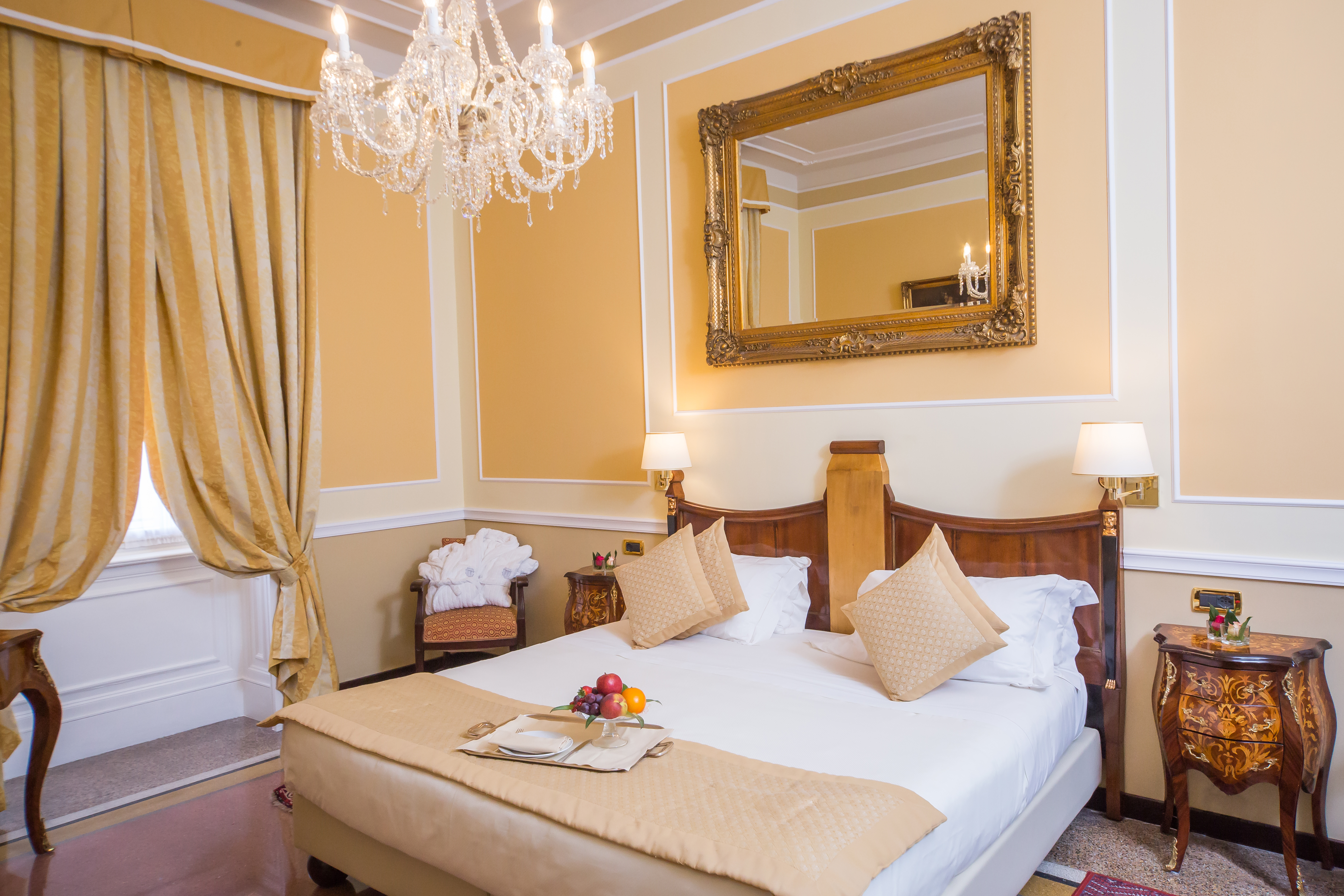 Hotel Bristol Palace Deluxe Room with warm, neutral decor, wooden antique furnishings, gold-framed mirror, and chandelier lighting
