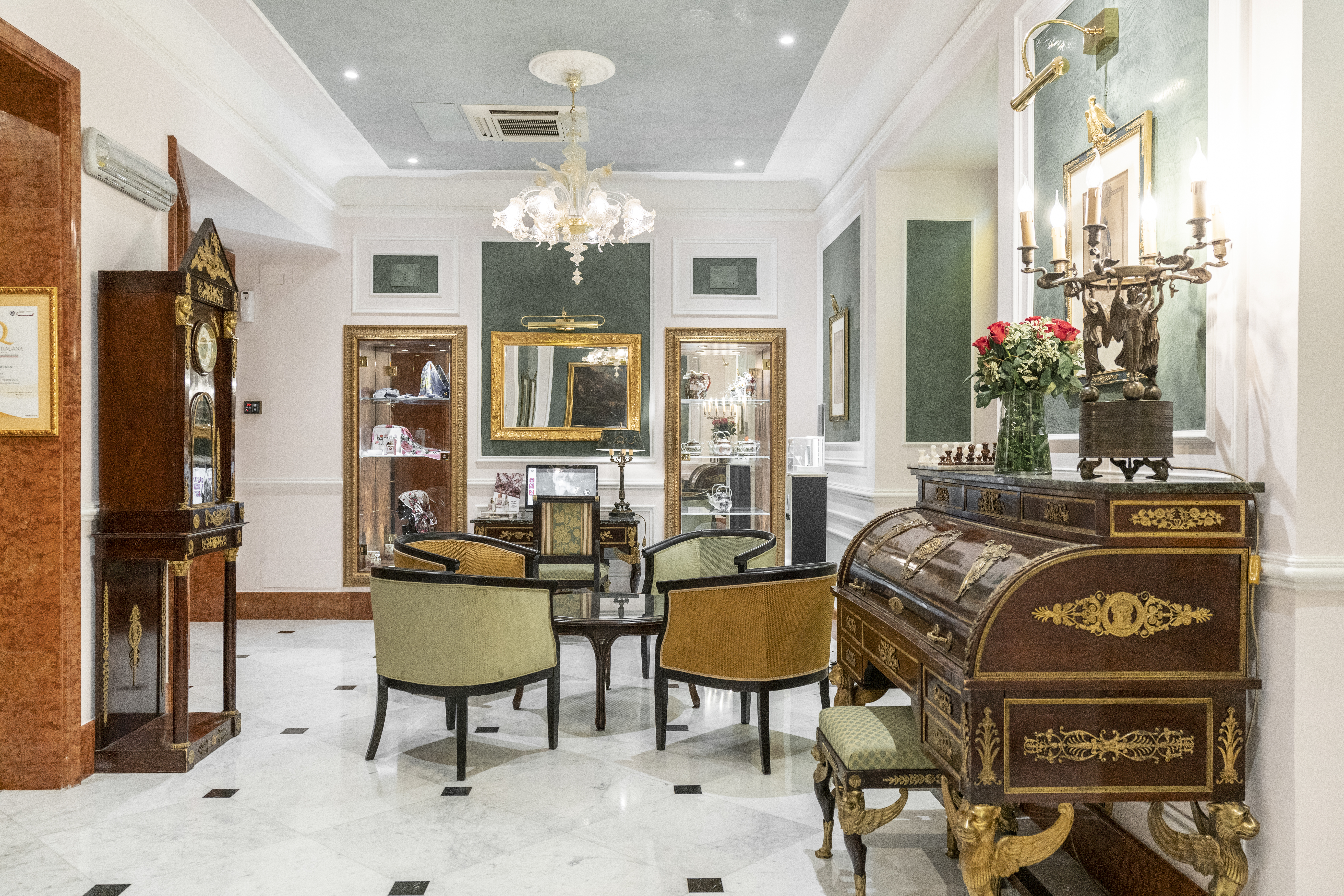 Hotel Bristol Palace lounge area with grand, antique furnishings, including a grandfather clock, teal accents on the walls, and chandelier-style lighting