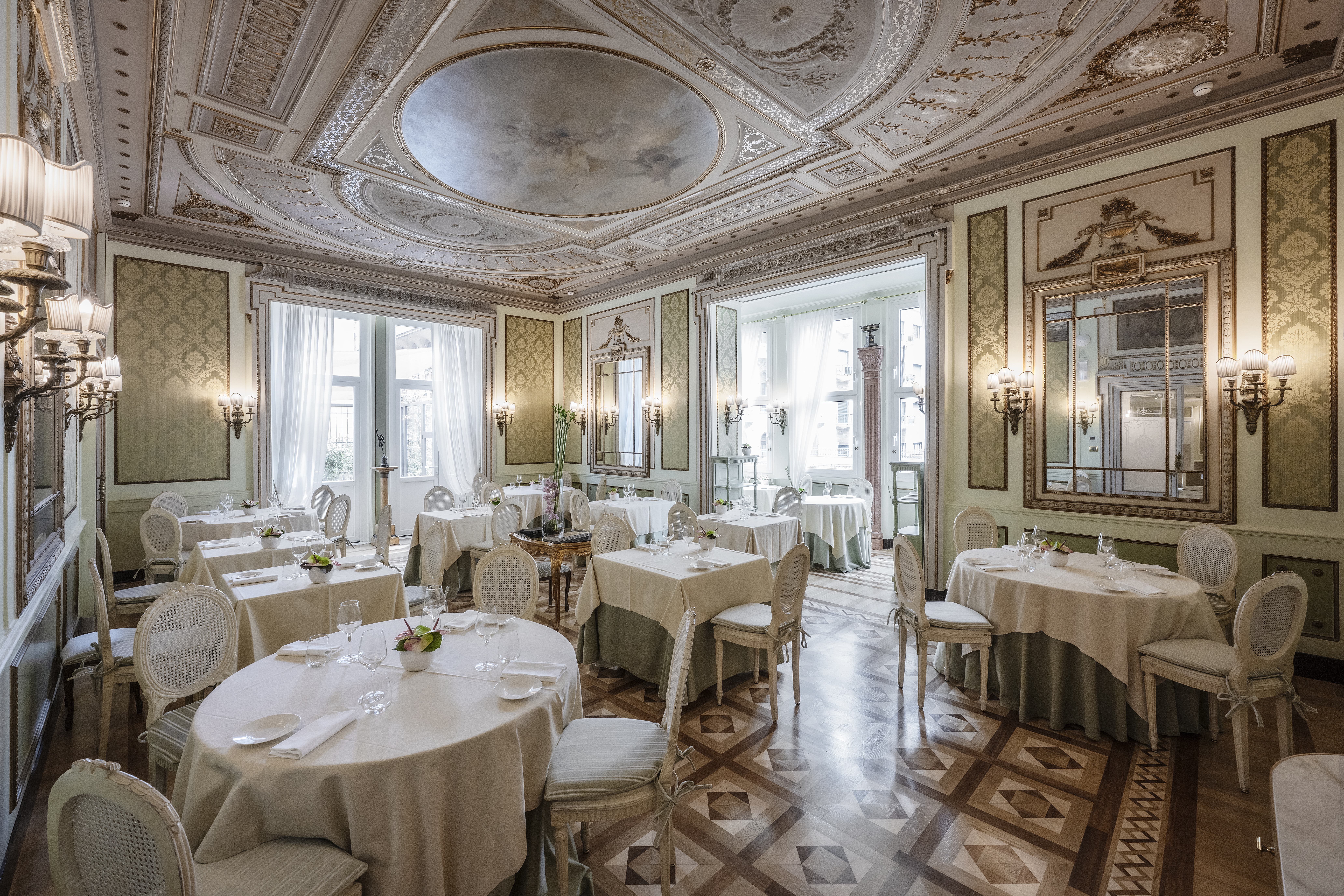 Hotel Bristol Palace restaurant with grand, ornate decor featuring gold and white, a patterned tiled floor, gold wall lamps, and plush high-backed dining chairs