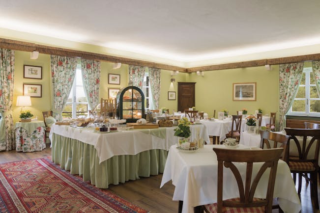 Green coloured walls and red rug with tables covered with white table cloths laid for breakfast at La Meridiana