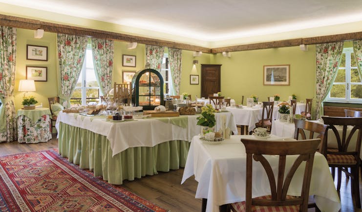 Green coloured walls and red rug with tables covered with white table cloths laid for breakfast at La Meridiana