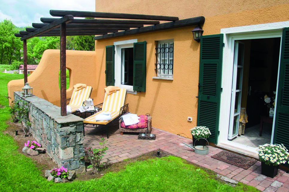 Garden patio with lounger chairs and grass outside open French window with green shutters at La Meridiana