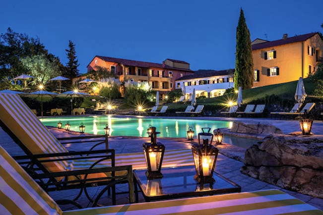 Pool with illuminated hotel buildings at night with cypress trees and lanterns on tables at La Meridiana Liguria