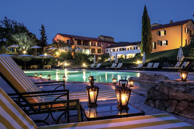 Pool with illuminated hotel buildings at night with cypress trees and lanterns on tables at La Meridiana Liguria