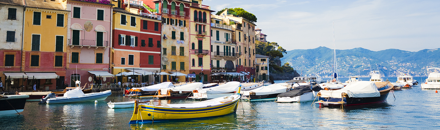 Coloured houses of pink and red on side of sea with boats moored on water