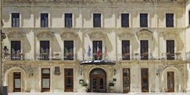 Facade in beige stone with long windows on three floors of the Patria Palace Lecce