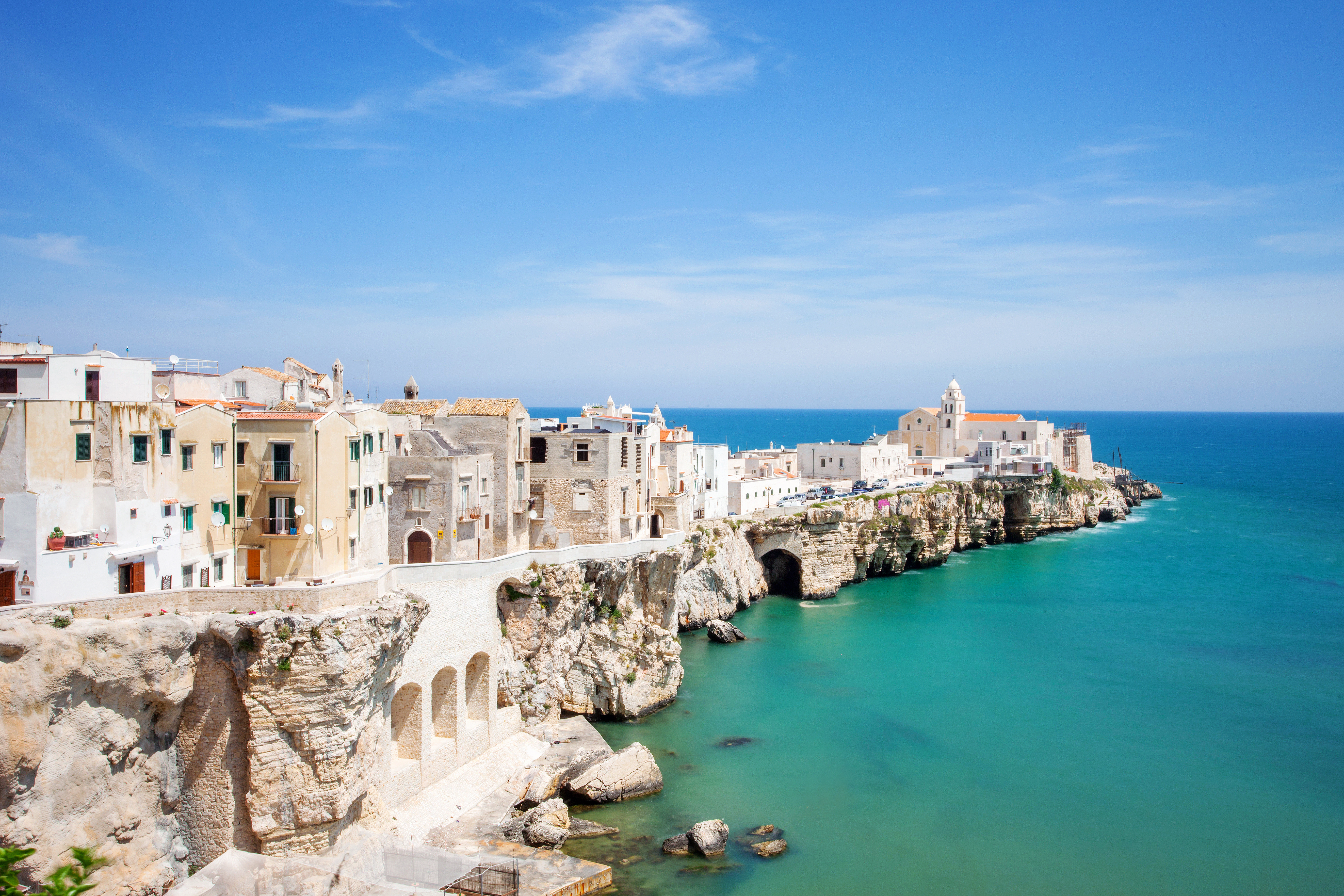 Line of white houses on white cliffs above emerald sea at Vieste in Puglia