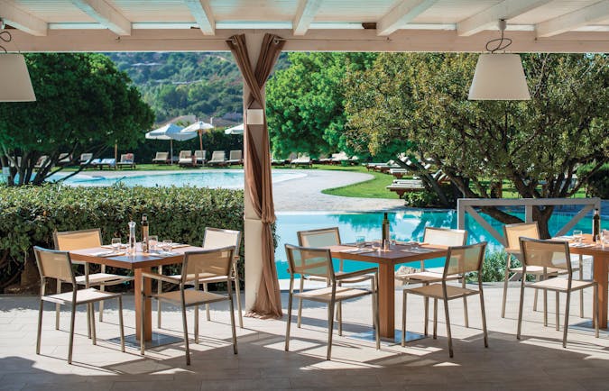 View of the Club house pool restaurant, showing wooden tables and chairs set up beneath a veranda overlooking the pool