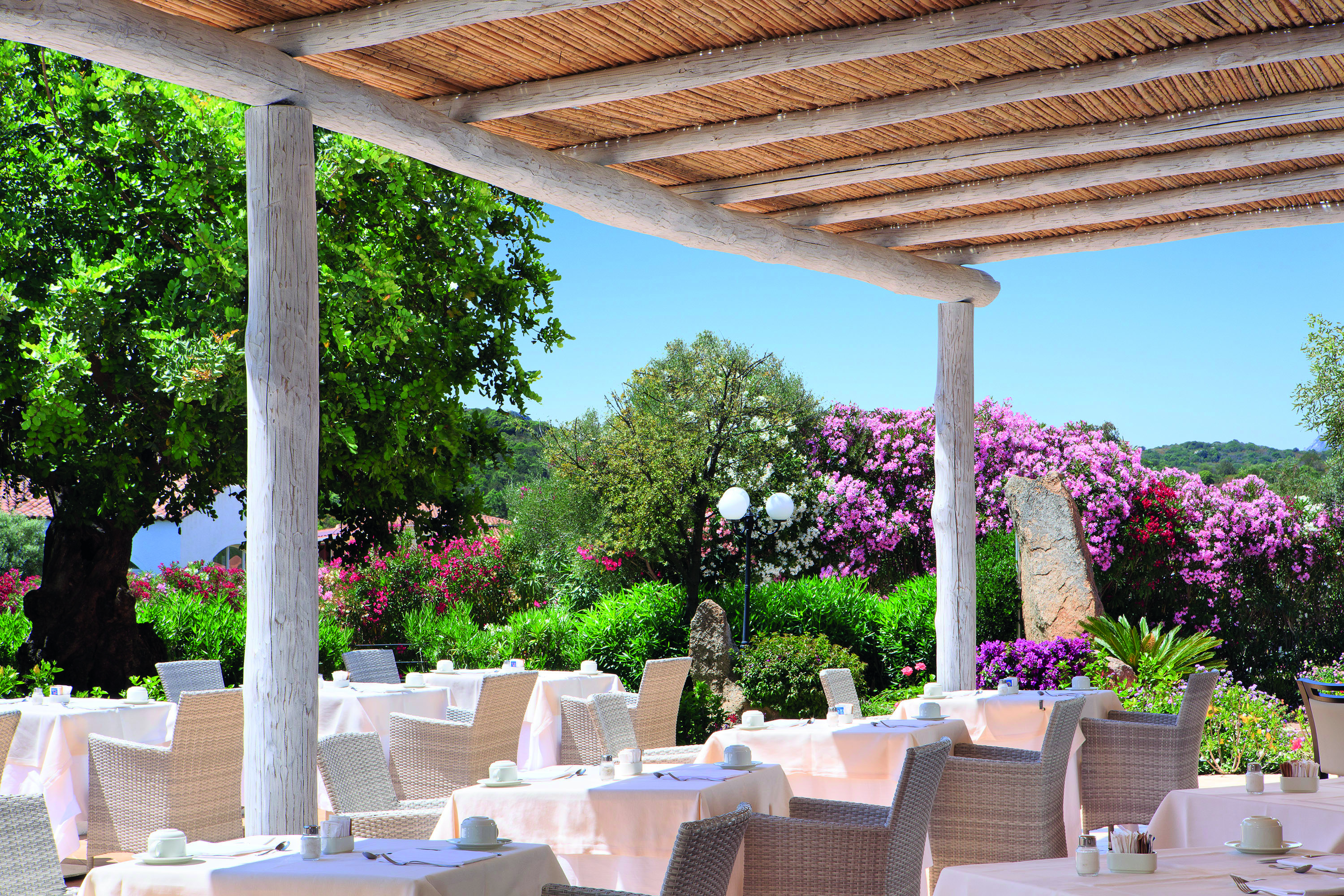 La Rocca Sardinia outdoor dining restaurant surrounded by trees flowering bushes